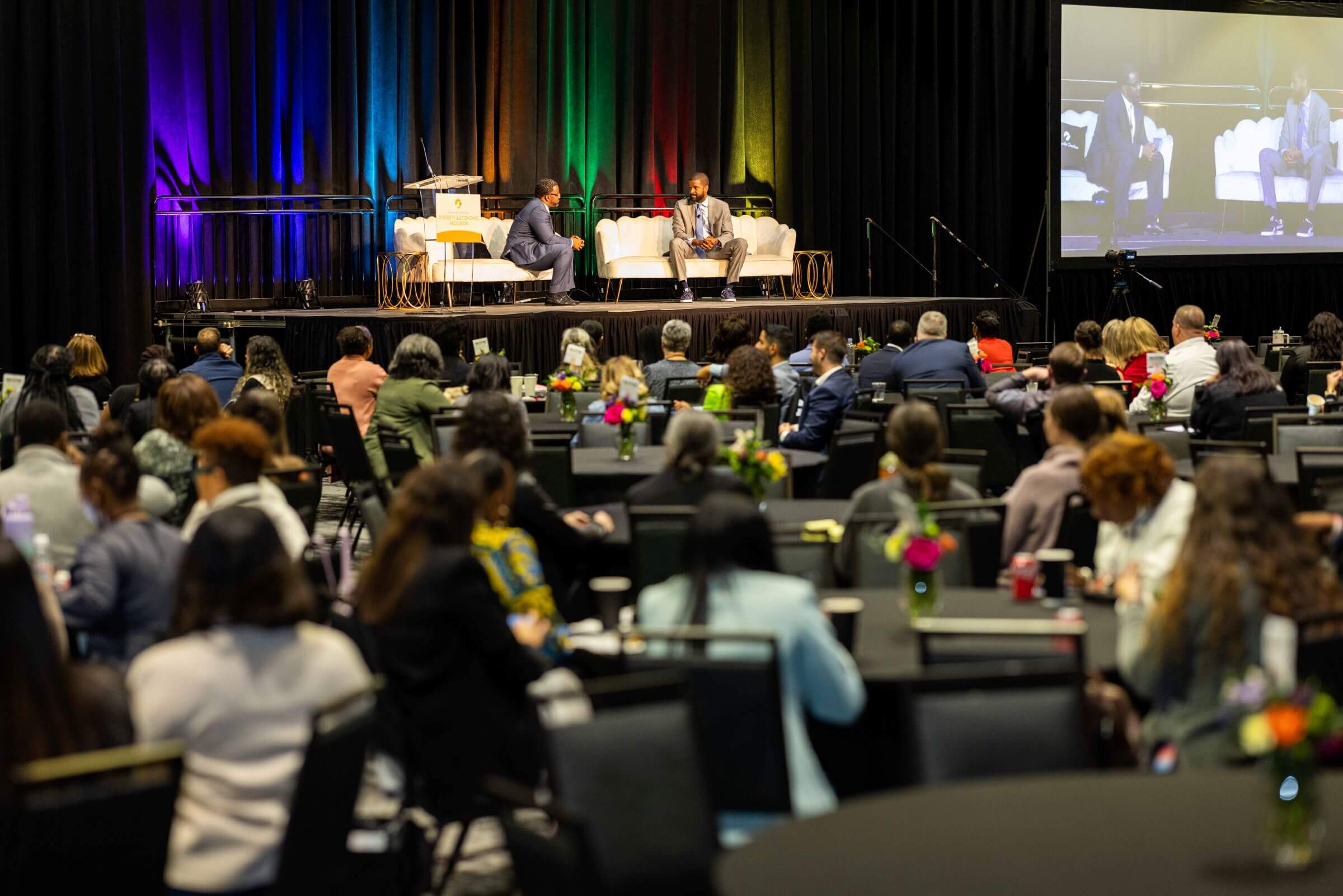 Panel discussion on stage before an audience seated at round tables