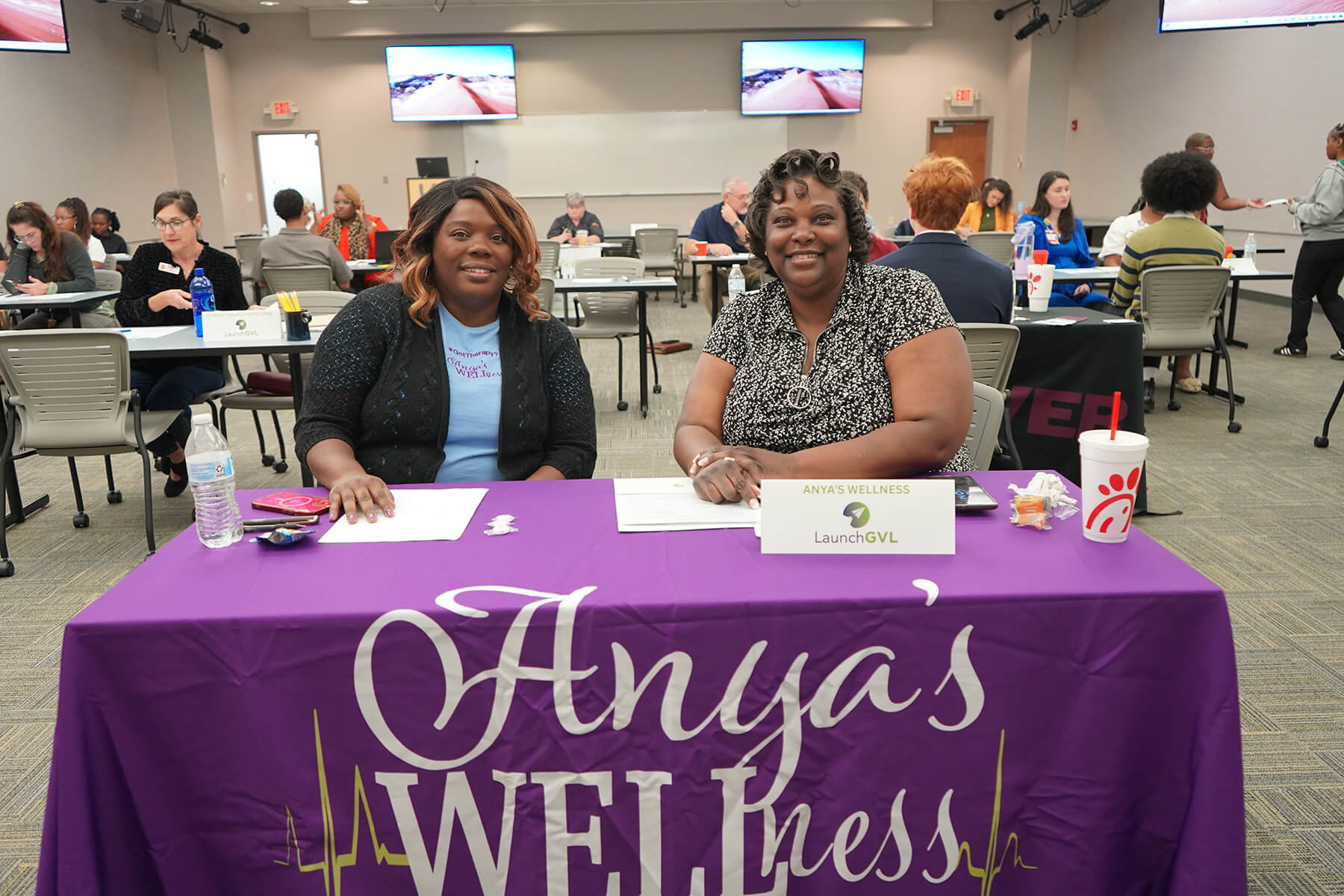 Exhibitors seated at an Anya's Wellness table at a business expo