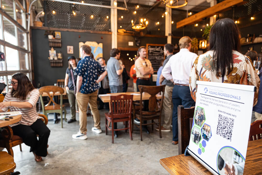 Attendees mingling at a Greenville Young Professionals event with a QR code sign in the foreground