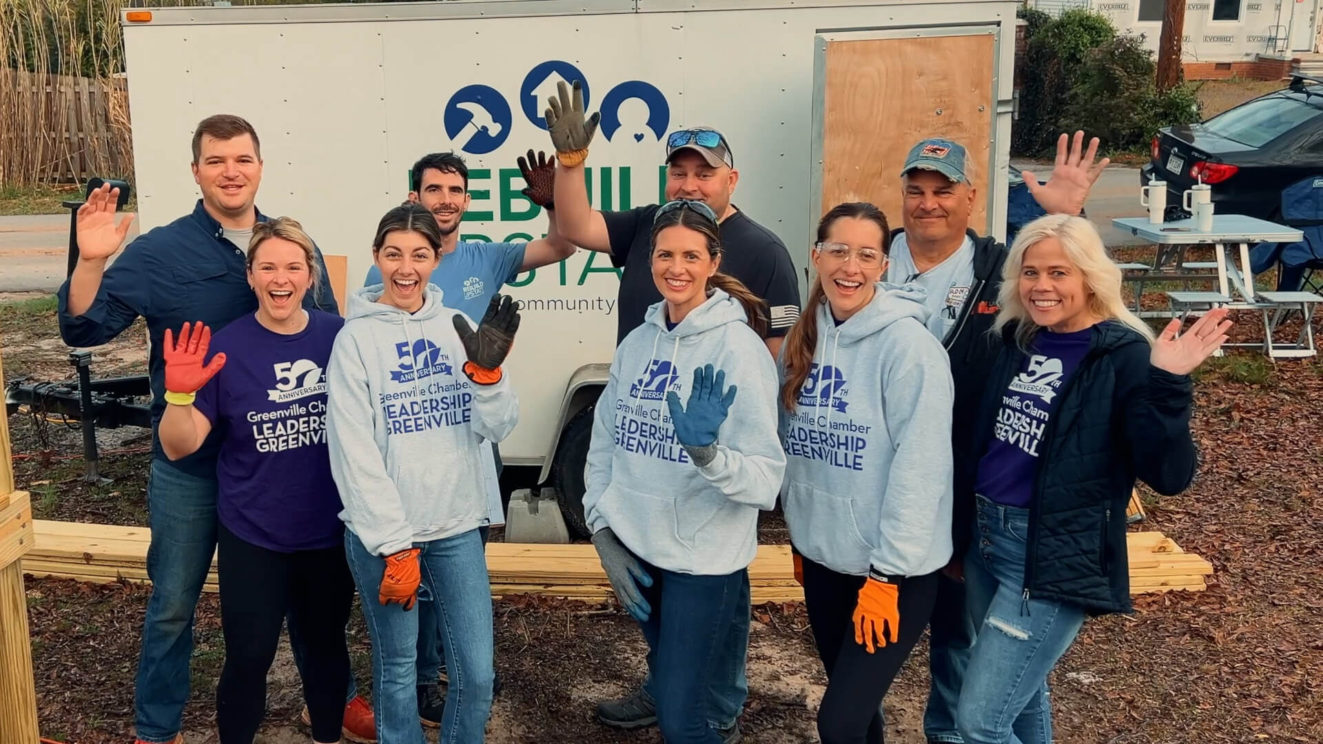 Volunteers in matching shirts waving and smiling at a volunteer event