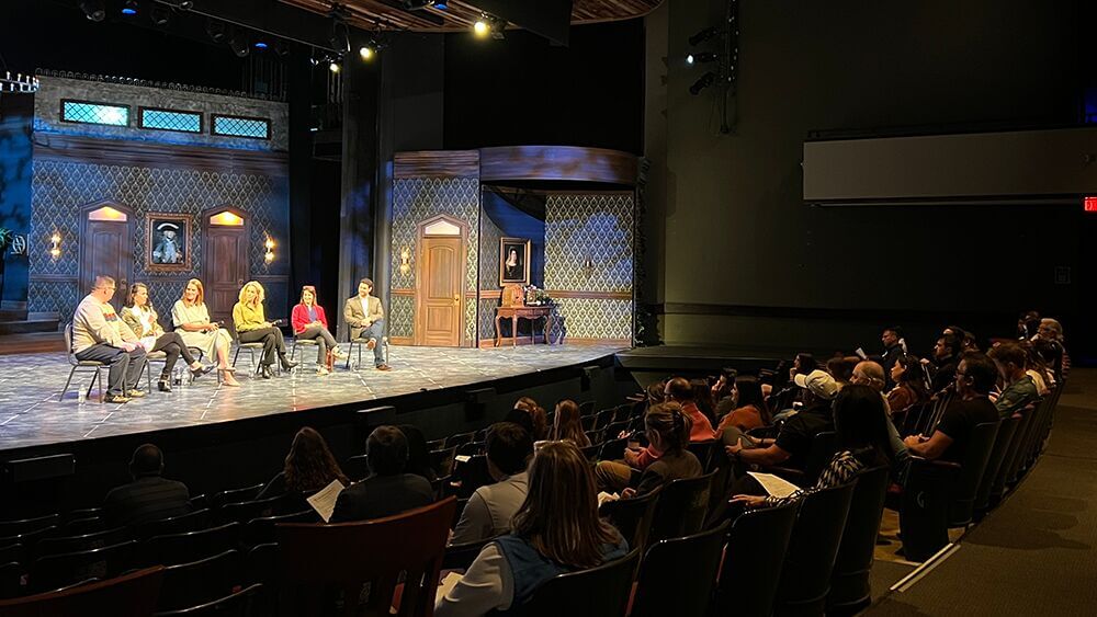 Panel of speakers seated on a theater stage in front of an audience
