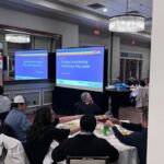 group of people sitting around tables watching presentation