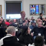 woman speaking at event with people in background sitting at tables