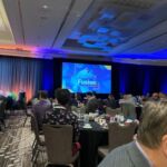 facility fusion on large screen in front of people sitting around tables
