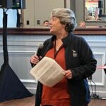 woman speaking into microphone in front of group of people