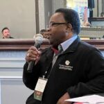 man speaking into microphone in front of group of people