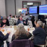 group of people sitting around tables watching presentation