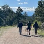 three people and a dog walking down trail