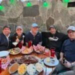 five people sitting around table of food getting ready to eat