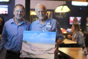 two men smiling and one holding a painting