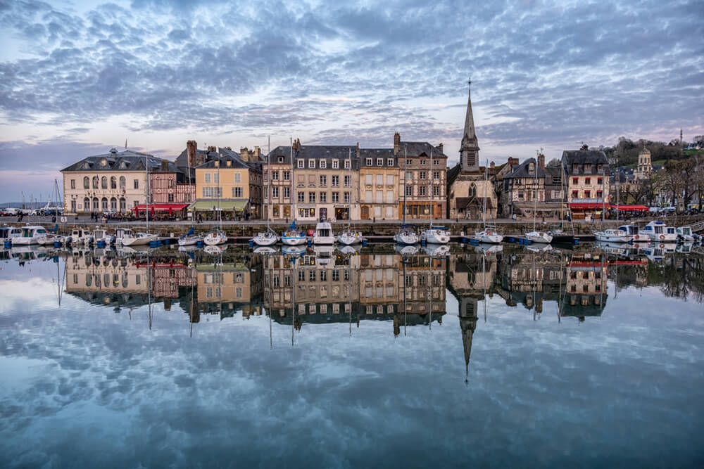 The port of Honfleur with the buildings reflecting on the water under a cloudy sky in France