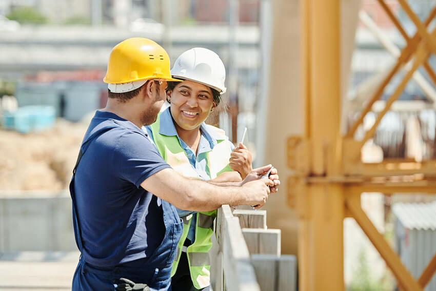 Two people dressed in construction safety gear and talking as they stand in the middle of a construction site.