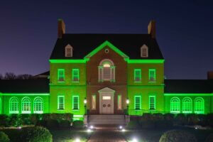 A photo taken at night of the Maryland Governor's Mansion, a brick multi-story building, illuminated in bright green lights to help recognize Maryland's veterans.