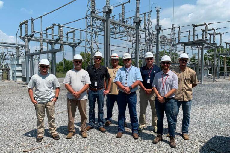 A group of educators participating in the Maryland Chamber Foundation's Teacher Externship Program alongside employees from their host company standing in a group in front of large electrical transformers wearing safety equipment.
