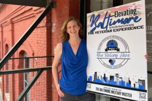 Maryland Rising Star podcast guest Katie Kilby holding a sign promoting her organization, Reveille Grounds, in Baltimore.