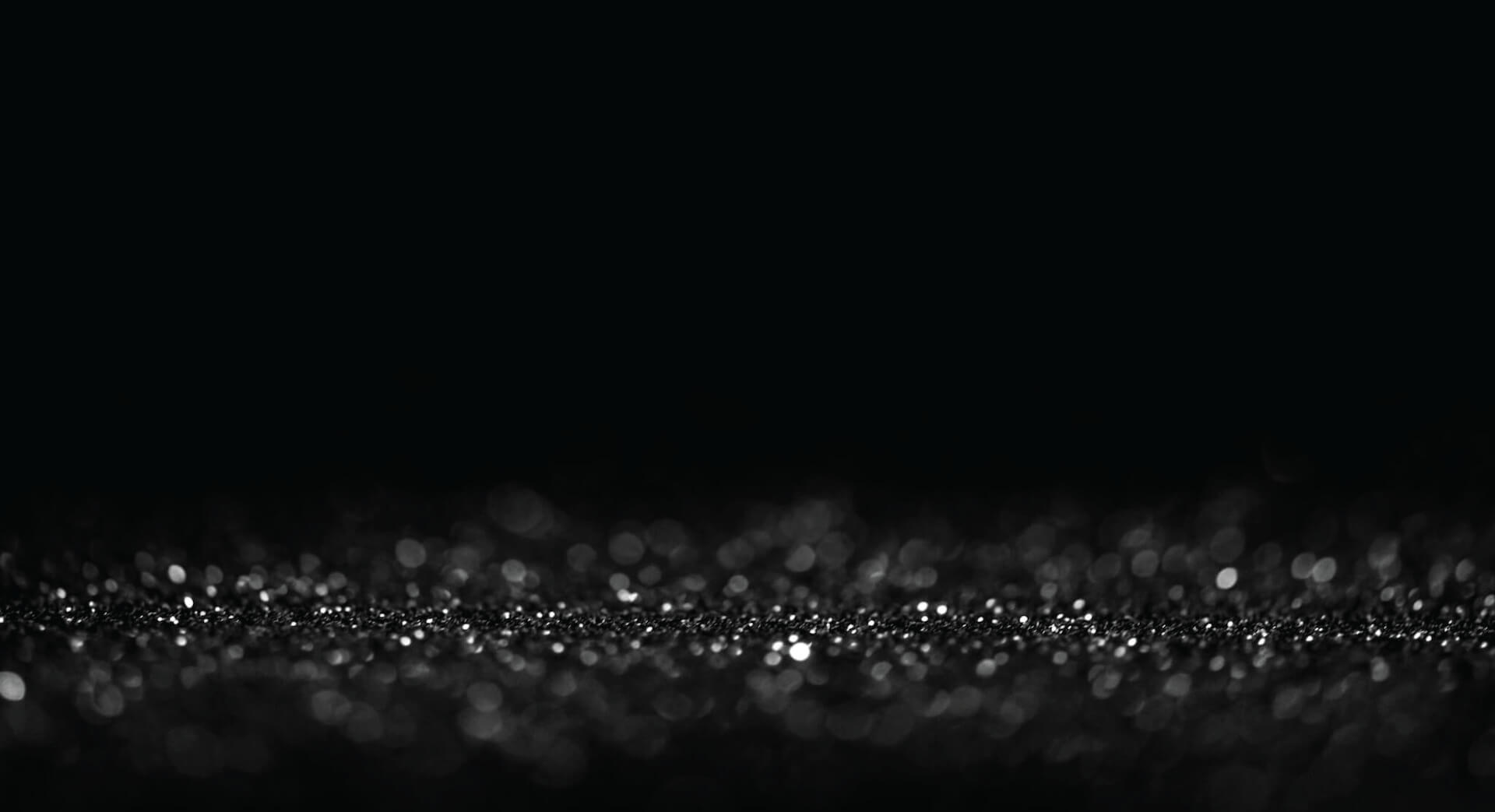 A black background graphic featuring clusters of silver speckles of confetti.