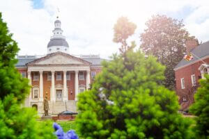 West facade of the Maryland State House in Annapolis on a cloudy spring day with flowers and trees appearing in the foreground.