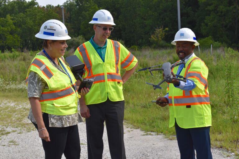 A pair of teachers wearing safety vests join an engineering company employee who is demonstrating how drone technology is used in their projects