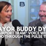 Chamber president/CEO Betsy Gardner, a woman with brown hair in a white jacket, sits besides Orlando Mayor Buddy Dyer, a man with salt and pepper hair and beard in a plaid suit jacket and white shirt.