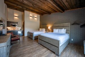 A cozy hotel room featuring two beds, wooden accents, and modern furnishings, with a kitchenette area visible.