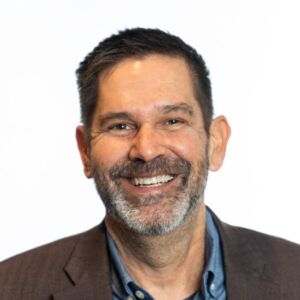 Dr. William Brown's headshot. He is wearing a brown blazer and blue shirt.