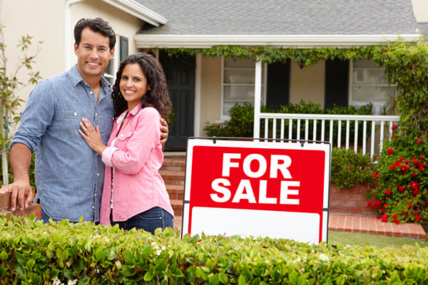 Hispanic couple outside home with for sale sign