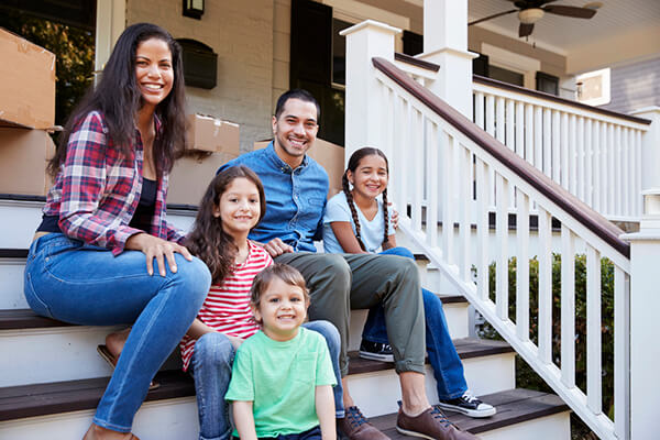 Family Sitting On Steps Of New Home On Moving In Day