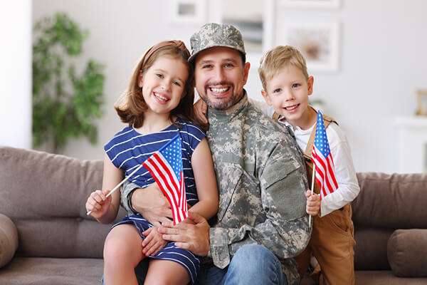 Portrait of happy american family father in military uniform and cute little kids son and daughter with flag of United States hugging and smiling at camera, male soldier dad reunited with family at home