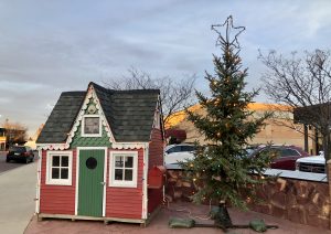 Small Red and Green cabin and large christmas tree next to it.