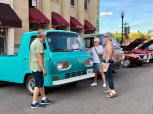 People admiring teal-colored ford econoline in front of historic building.