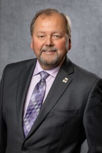 Smiling businessman in  grey suit with light purple shirt and geometrical purple tie. 