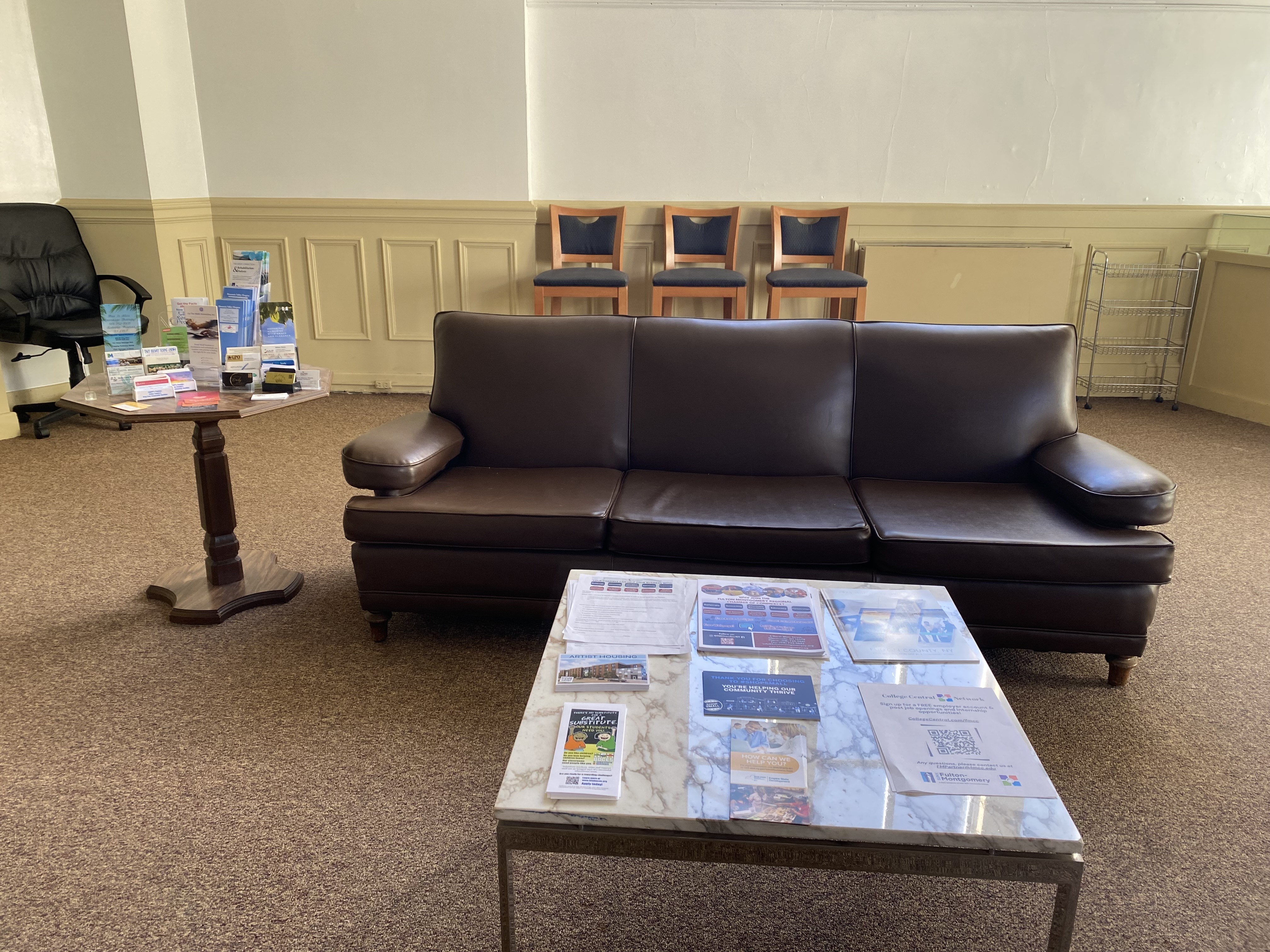 chamberGallerySeatingOct2025 Image of small seating area in the chamber lobby. To the left of the couch is a table with brochures and contact cards displayed and in front is a table with brochures and papers on top.
