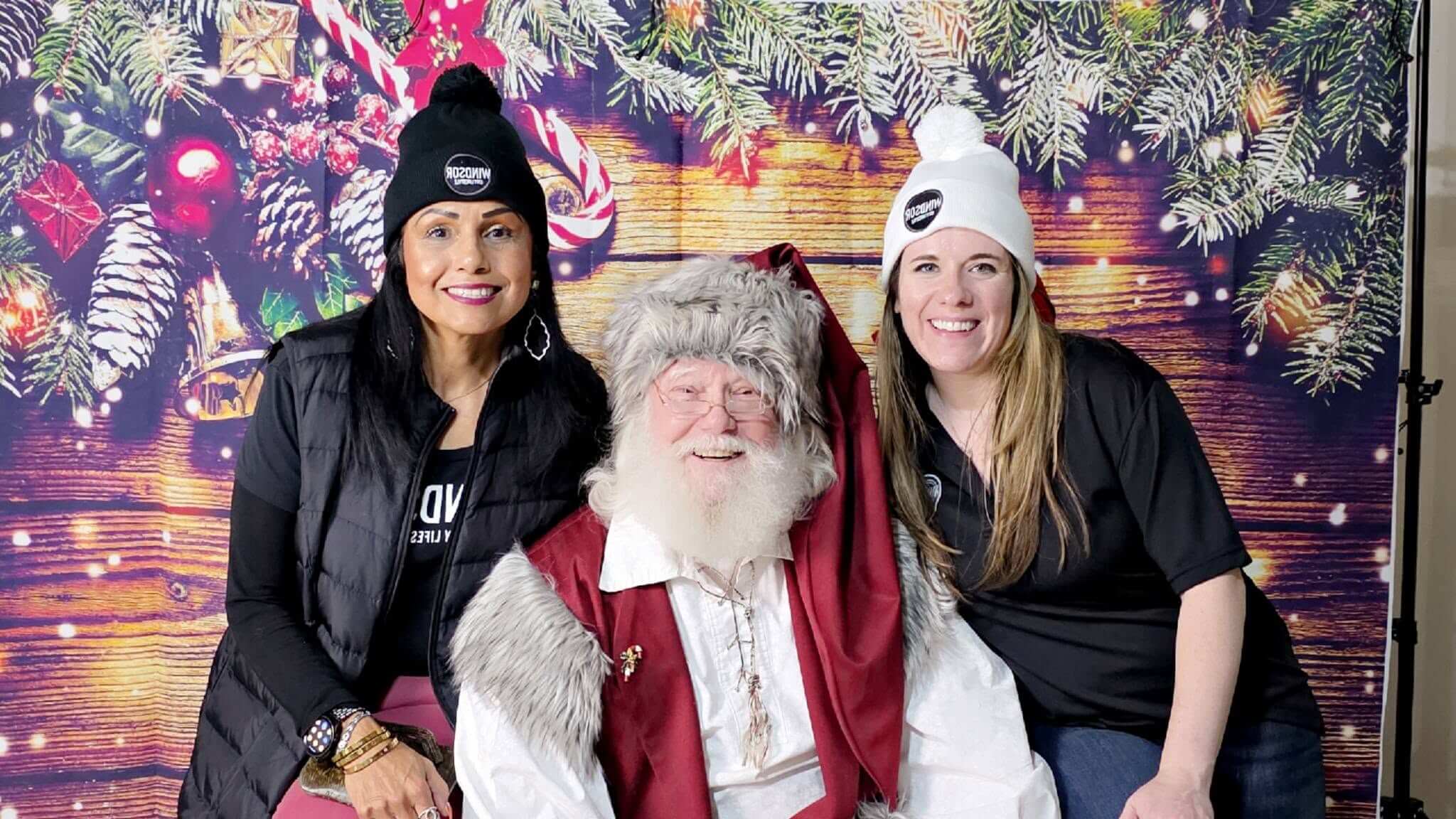 Two women on either side of Santa Claus with a holiday background