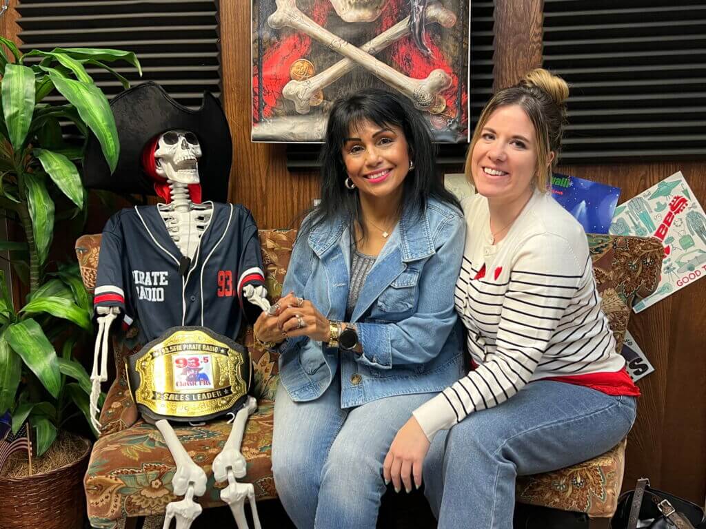 Two women sitting on a couch next to a pirate skeleton