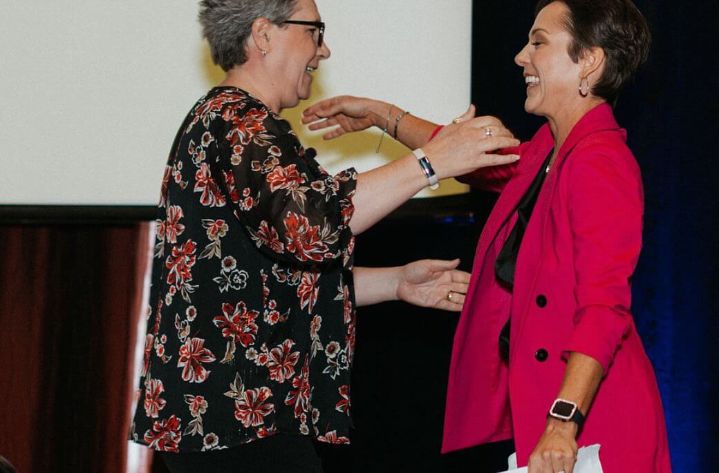 Two women go to hug on stage