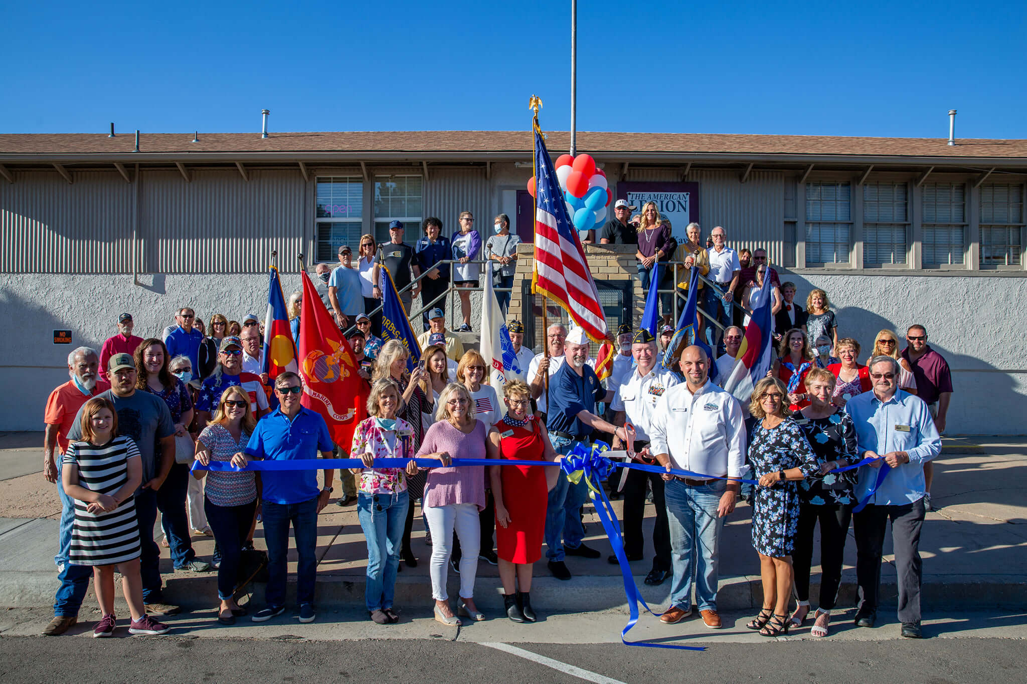 Large group of people with an American Flag standing behind ribbon.
