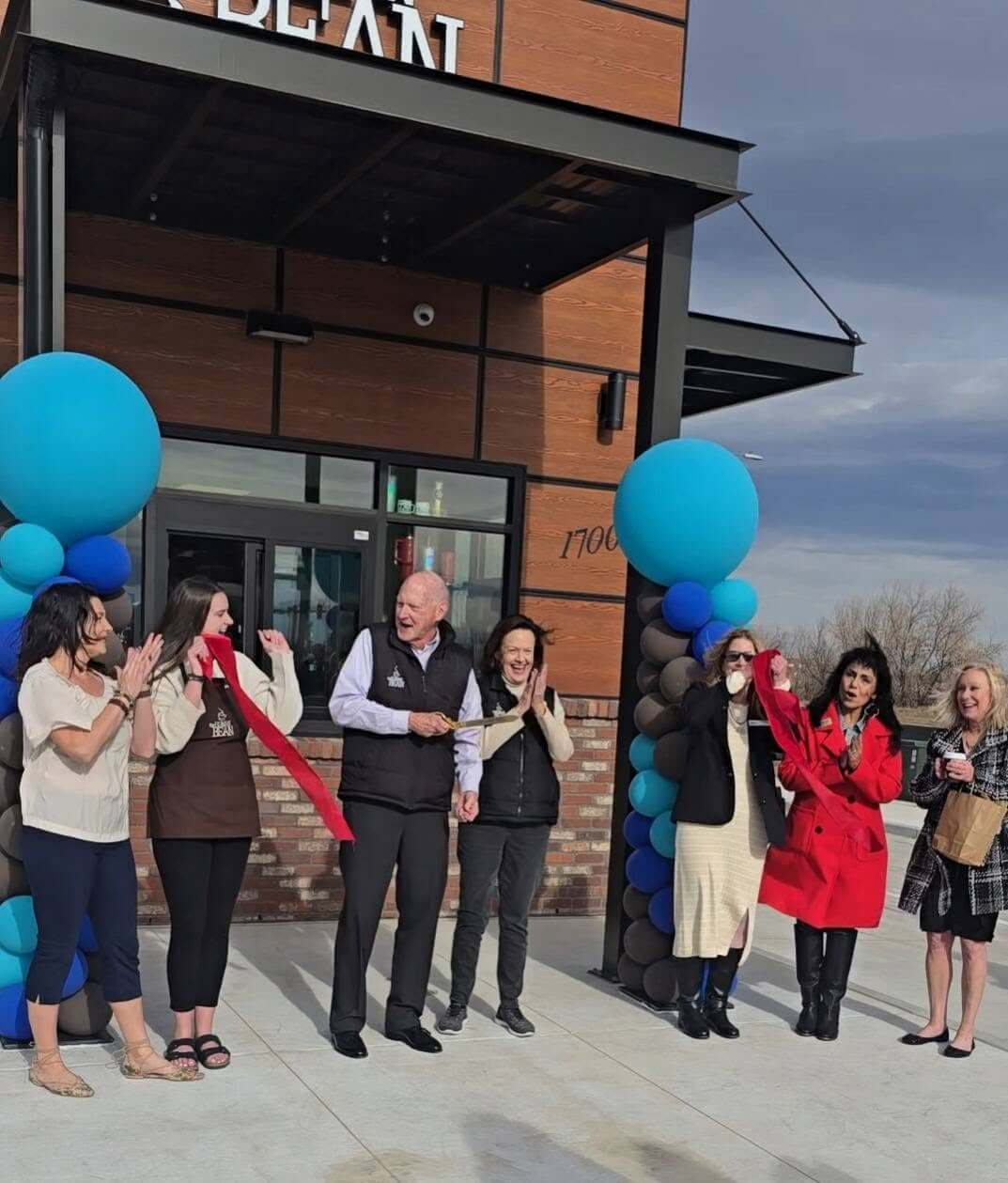 Several people cheering surrounded by balloons in front of Human Bean Coffee Drive Thru