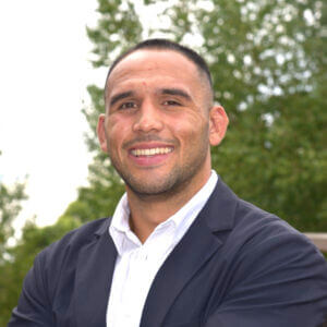 Man similing and wearing a button up collared white shirt with a suit jacket over.