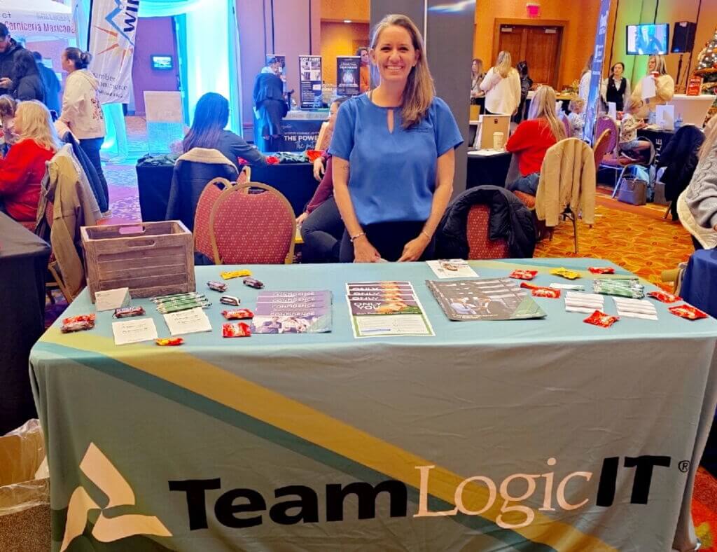 Woman in a blue top standing behind a table that says Team Logic IT