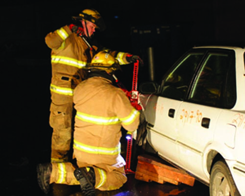 2 fireman in training using equipment on a car
