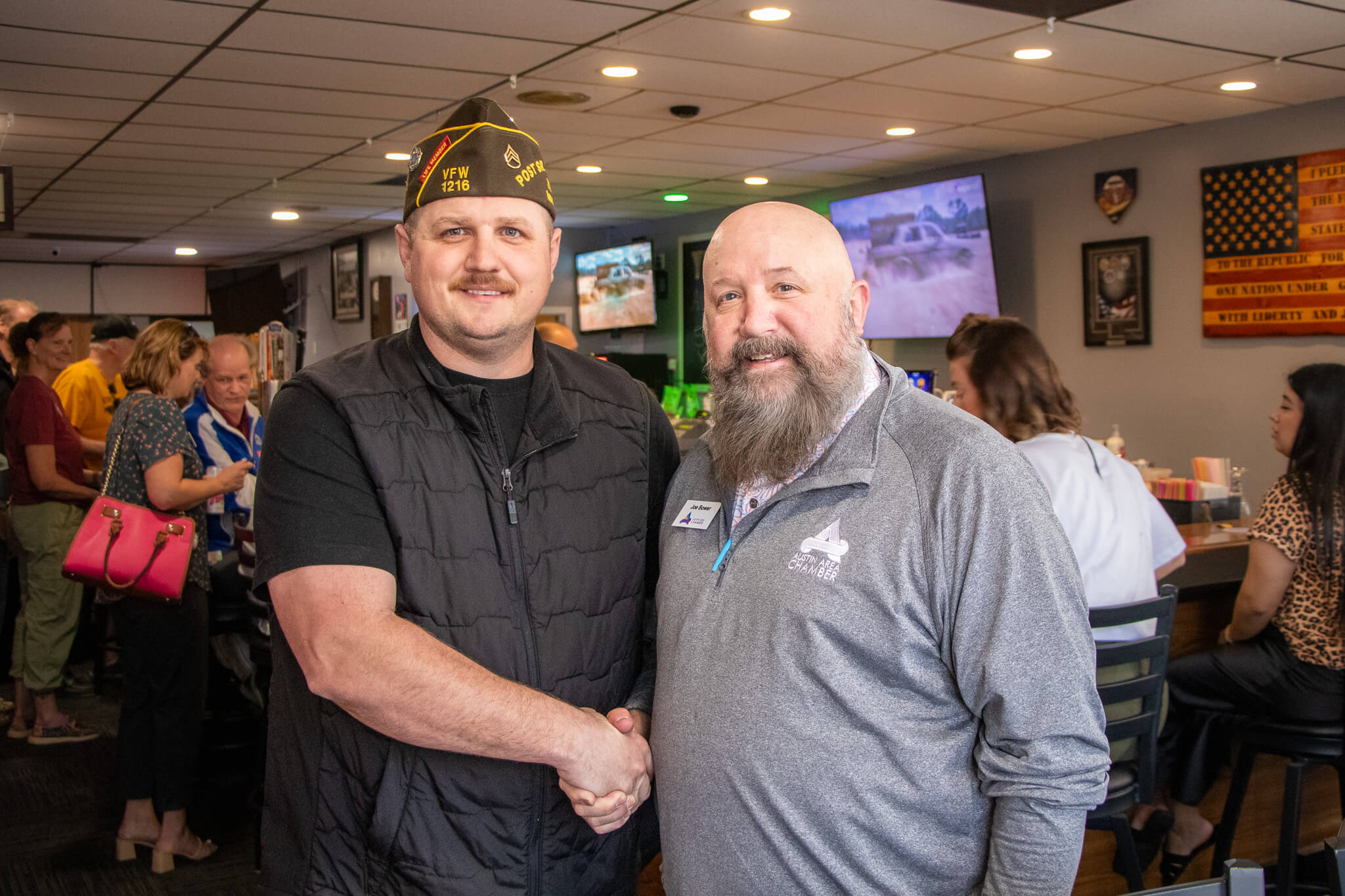 Joseph Bower, President/CEO of the Austin Area Chamber of COmmerce shaking hands with Justin Hutchinson from the VWF in a crowded bar.