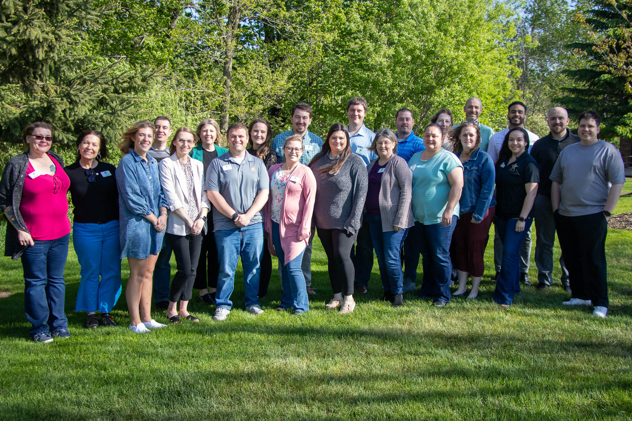 The 2025-2026 cohort standing outside on a fresh cut lawn sunny day. The background is filled with greenery. There are two rows of of the Cohort with 12 people in each row.