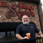 Bob Karas of the Karas restaurant groups holding a drink infront of the Village Squire
