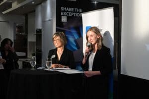 Two women speak in front of a banner.