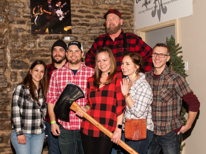 Several people wearing flannel standing together while woman in front holds axe