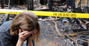 Woman holding head in hands outisde fire damaged home