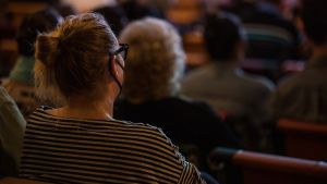 A Point-of-view photo from within an audience, with others looking up at a stage offscreen.