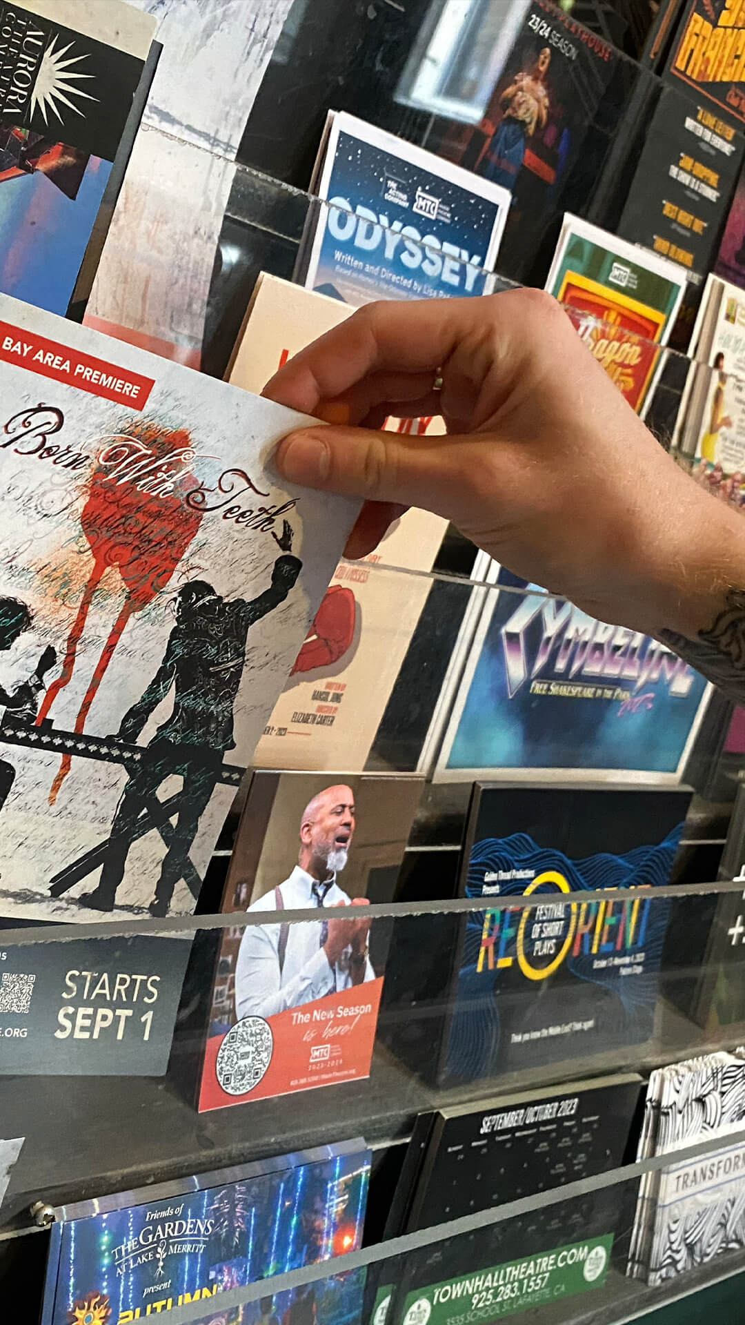 a white hand picking up a postcard off a full postcard rack