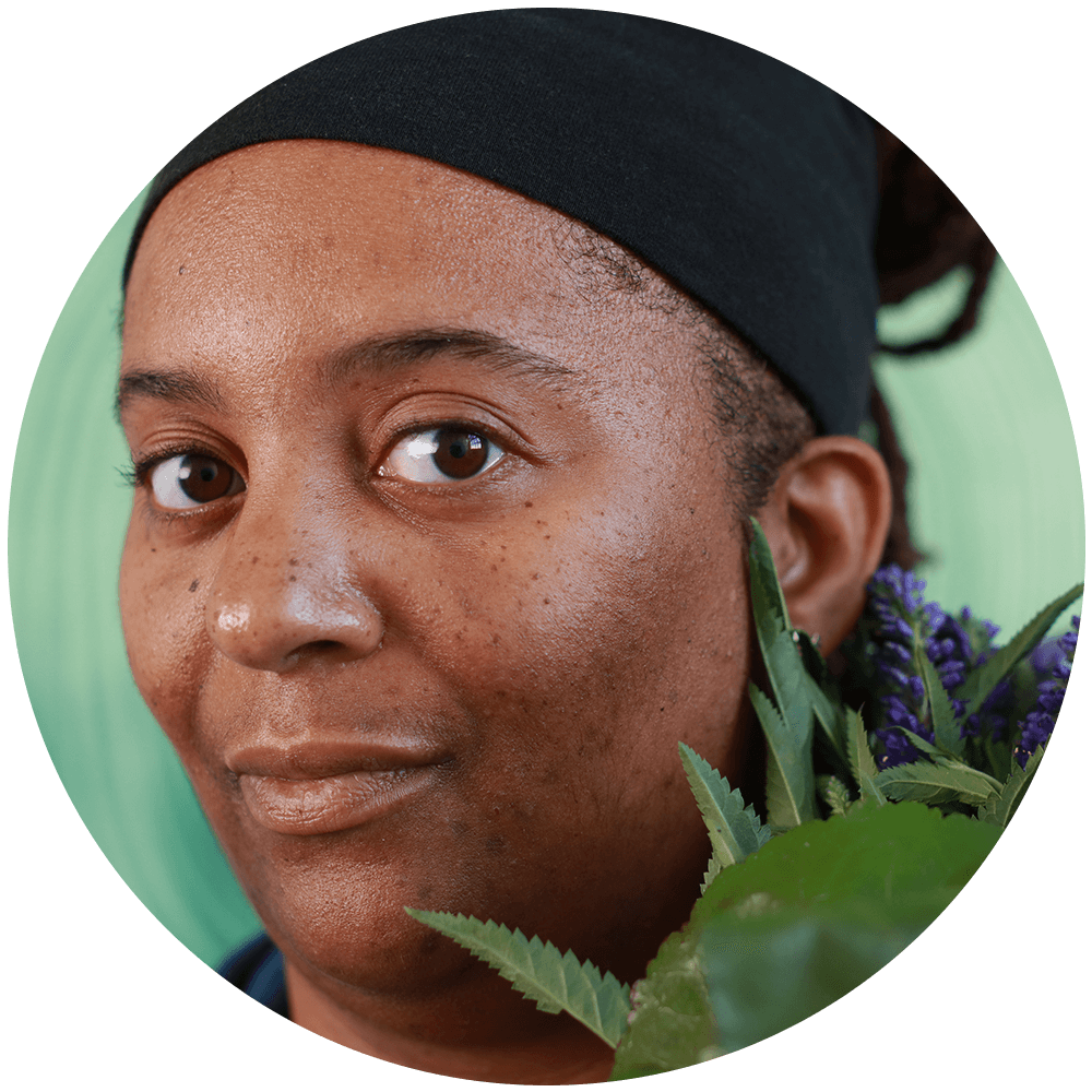 African American woman with black headband facing center with a bouquet of lavender on her right shoulder.