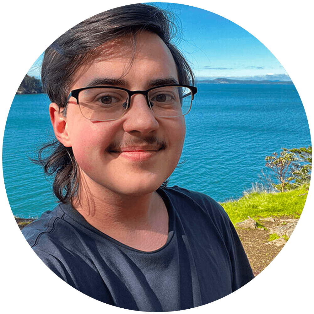 Selfie of a white Latine person smiling with a sunny bay view in the background.